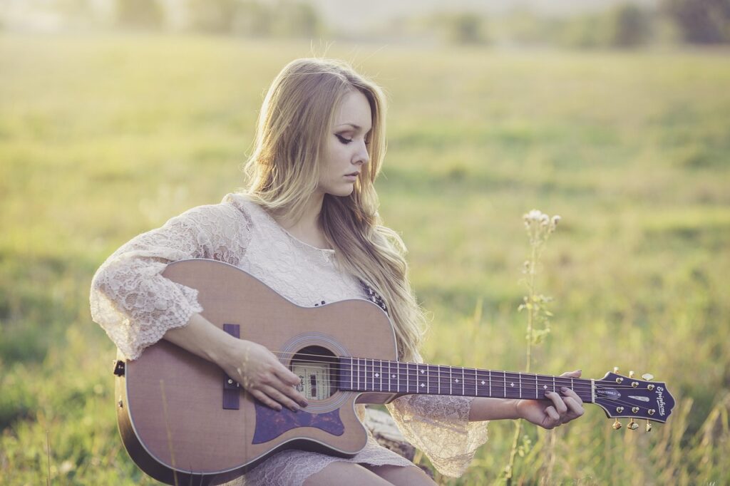 Uma mulher sentada no chão tocando um violão. A luz do sol  reforça a ideia da música como uma ferramenta de autocuidado e cura emocional.