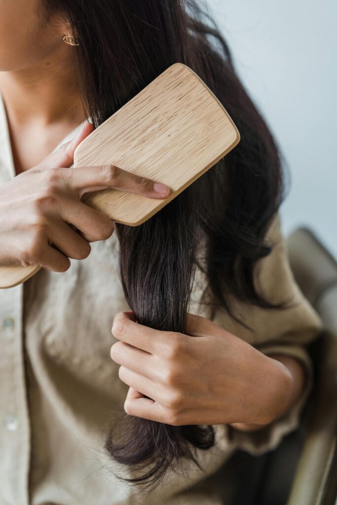 Mãos femininas escovando os cabelos, ilustrando a rotina de cuidados e saúde do cabelo