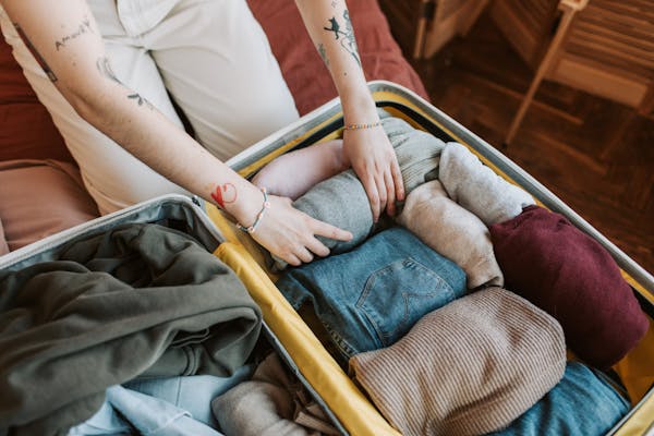 Vista aérea de uma mala aberta sobre uma cama. Dentro, roupas estão perfeitamente organizadas em rolinhos, ilustrando como montar a mala perfeita de forma prática.