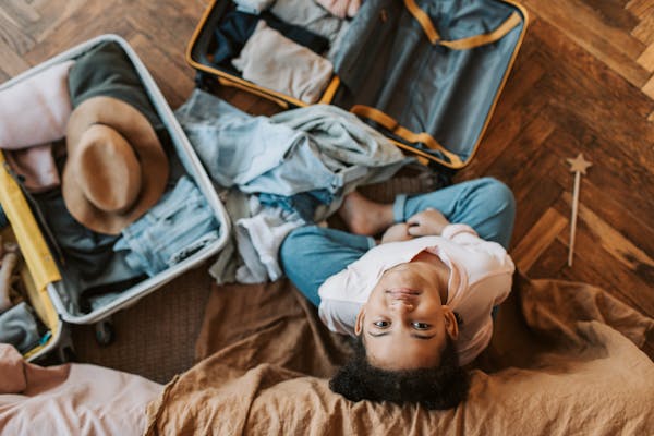 Uma mala aberta sobre um piso, revelando roupas leves e chapéu. As roupas estão dobradas de forma otimizada, transmitindo a facilidade de montar uma mala de verão para destinos ensolarados.