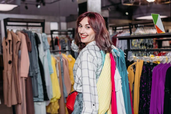 Close-up of a woman's hands thoughtfully browsing a clothing rack, representing smart shopping strategies to build a versatile and irresistible wardrobe.