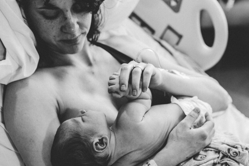 Mãe amamentando em uma poltrona confortável, trocando um olhar carinhoso com o bebê. A iluminação é suave, destacando o vínculo afetivo e a liberação de ocitocina durante o aleitamento materno.