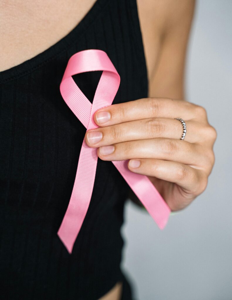 Mulher usando um laço rosa na blusa, simbolizando o apoio à campanha de prevenção ao câncer de mama.