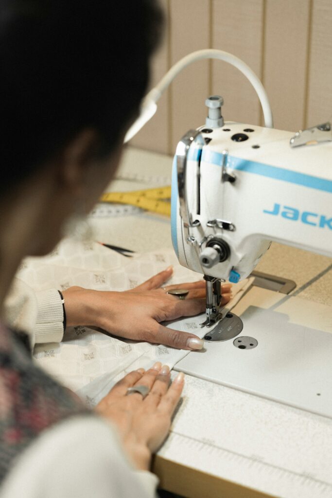 Mãos habilidosas de uma costureira guiando um tecido fino sob a agulha de uma máquina de costura vintage, em um ateliê iluminado.
