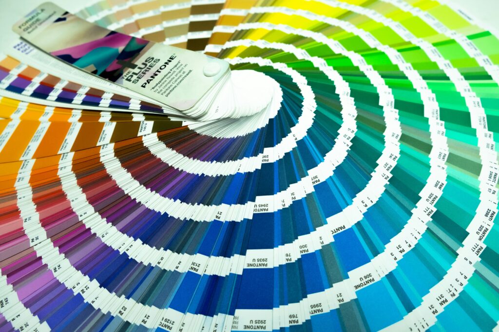 Close-up de um leque de cores da escala Pantone aberto, exibindo uma graduação de tons vibrantes e códigos de identificação técnica.