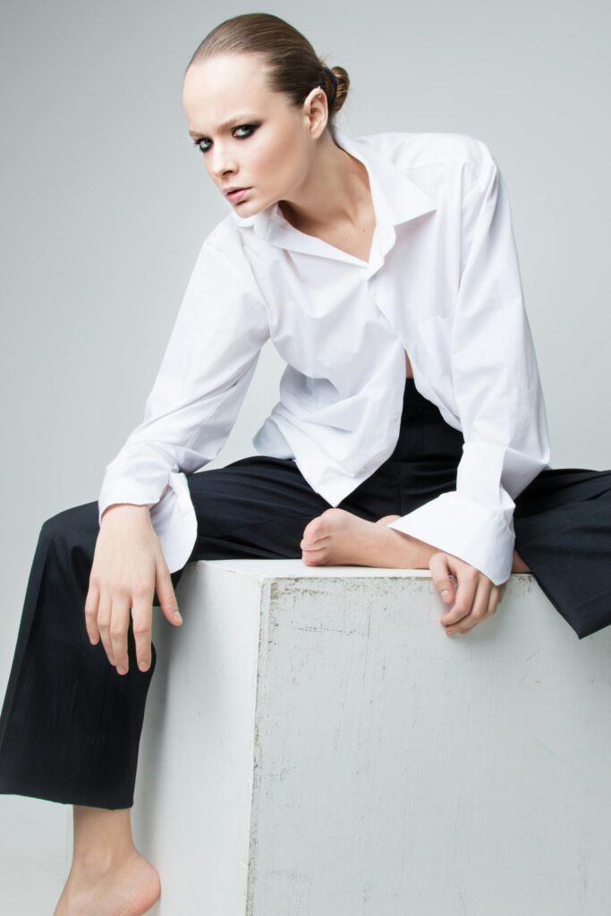 Mulher usando um look minimalista composto por uma camisa branca de alfaiataria e calças pretas, em um contraste clássico e elegante.